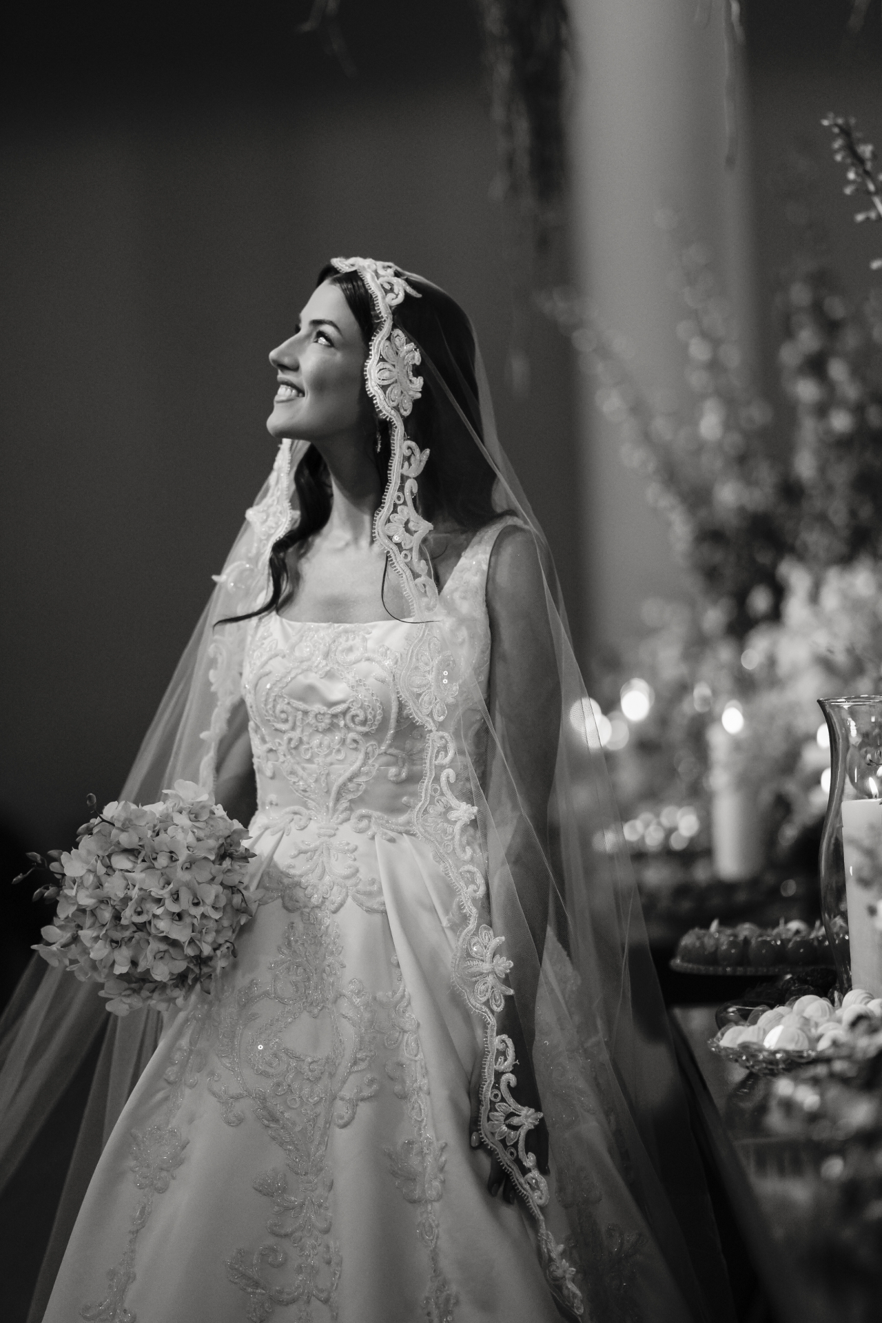Noiva sorrindo sob um véu de renda, em fotografia editorial em preto e branco