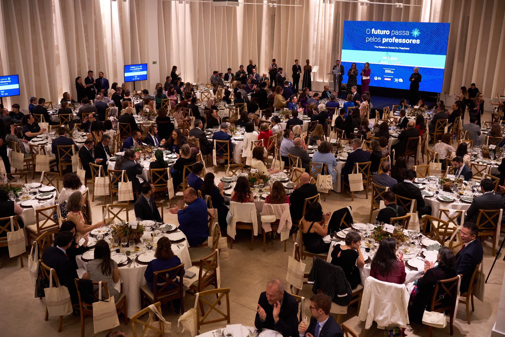 Vista do salão com convidados à mesa e palco ao fundo