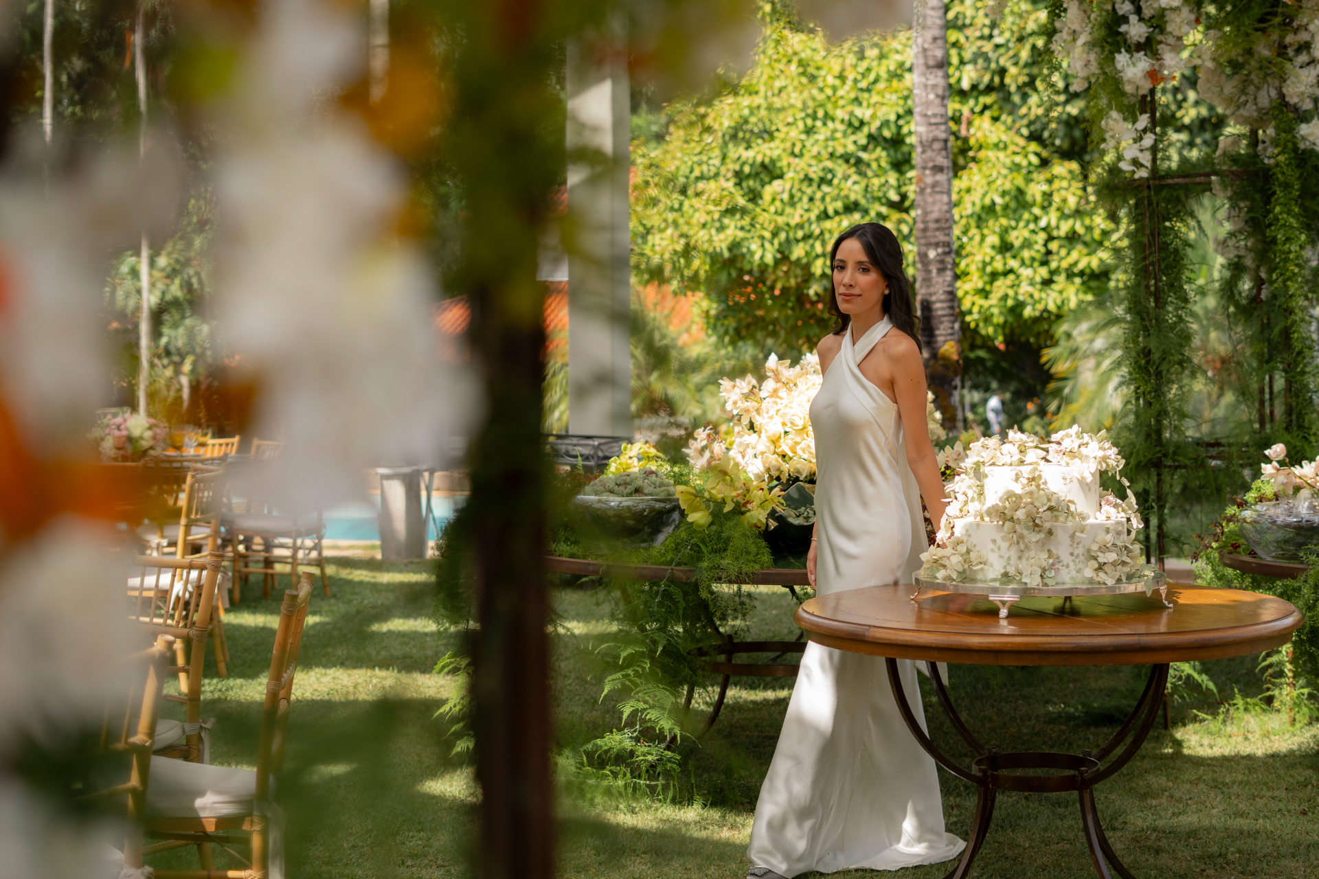 Noiva em vestido branco junto à mesa de flores no jardim